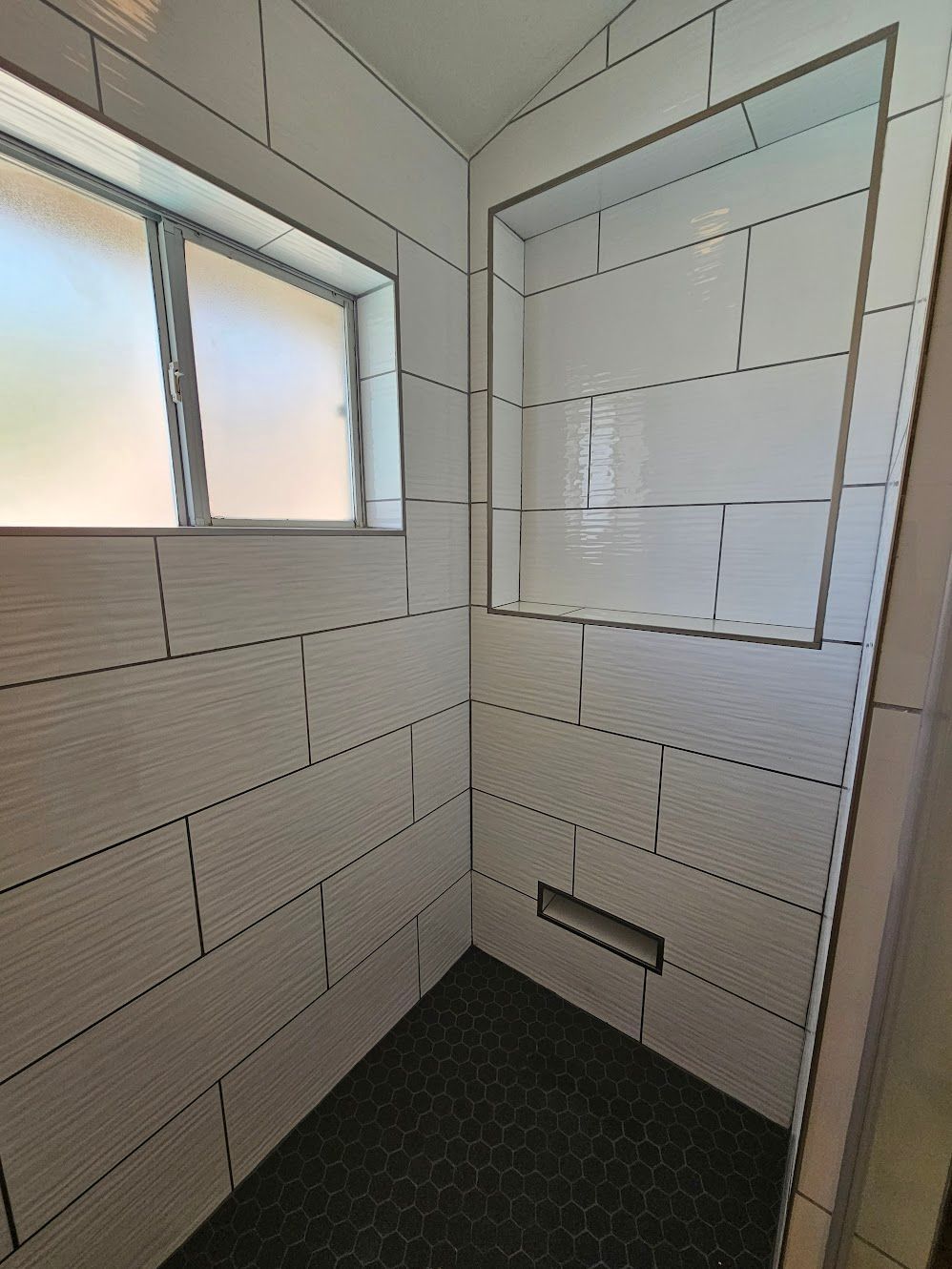 White tiled shower with a black hexagon tile floor and a built-in shelf.