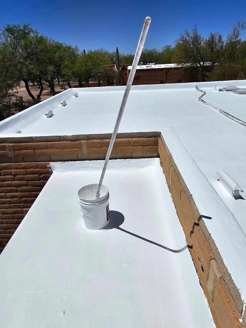 White-painted flat roof with a bucket and long handle. Sunny day, blue sky.