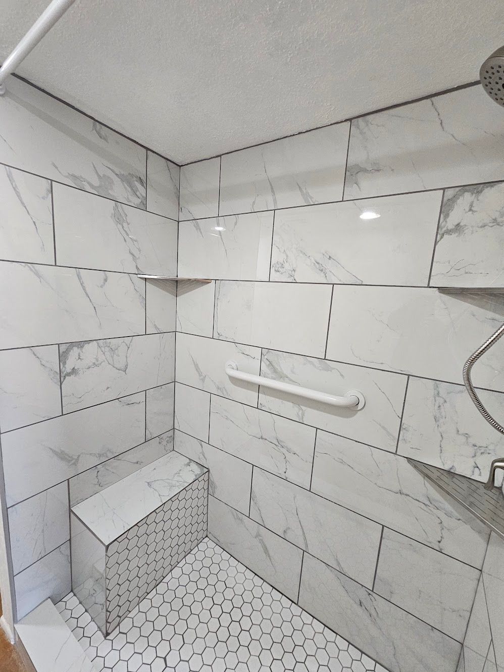 White tiled shower with built-in bench, shelves, and pebble floor.