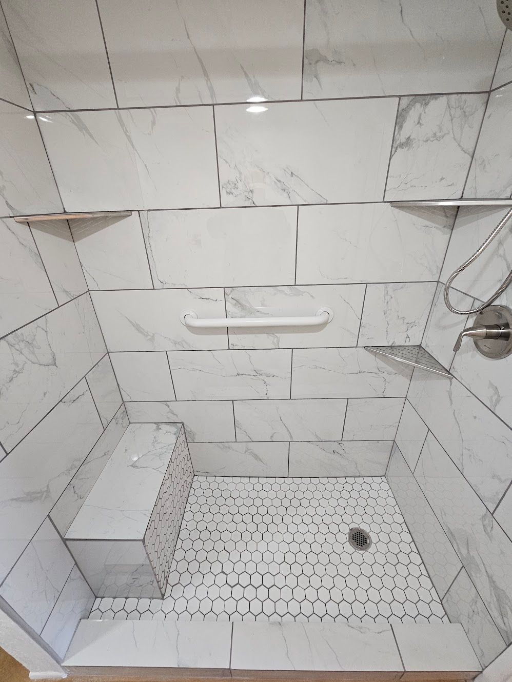 White tiled shower with built-in bench, shelves, and pebble floor.