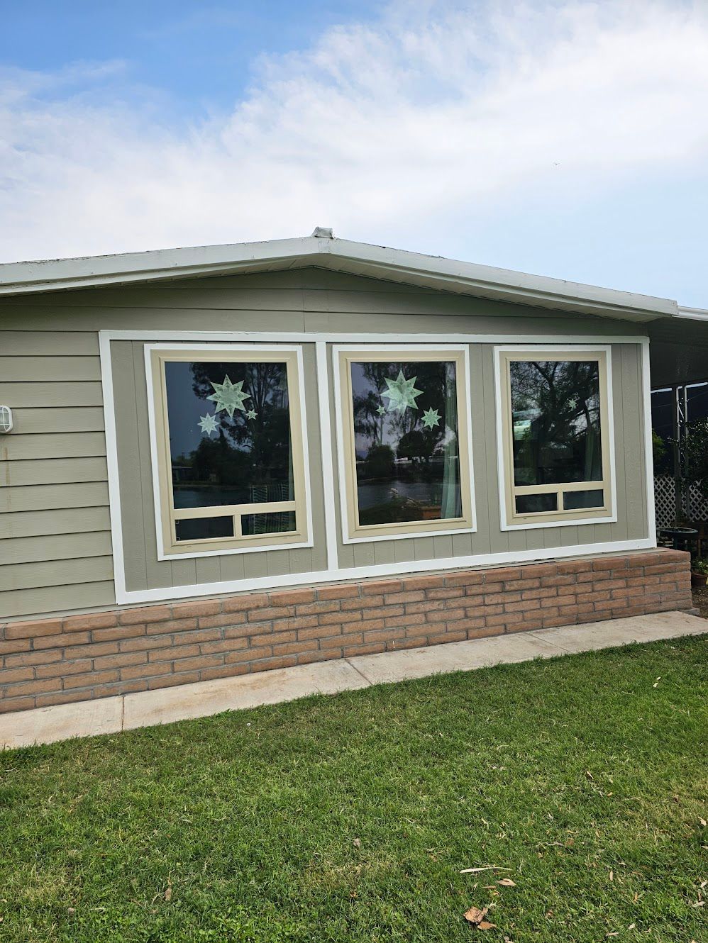 Three rectangular windows with decorations, on a light-colored building with a brick base, under a blue sky.