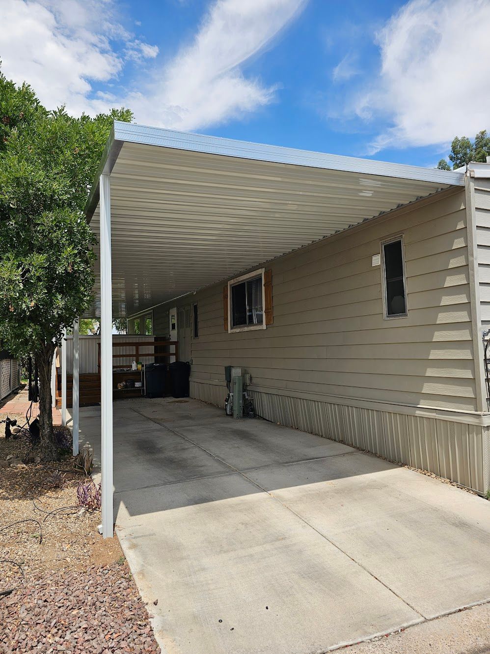 Carport attached to a beige mobile home with a concrete driveway, under a blue sky.