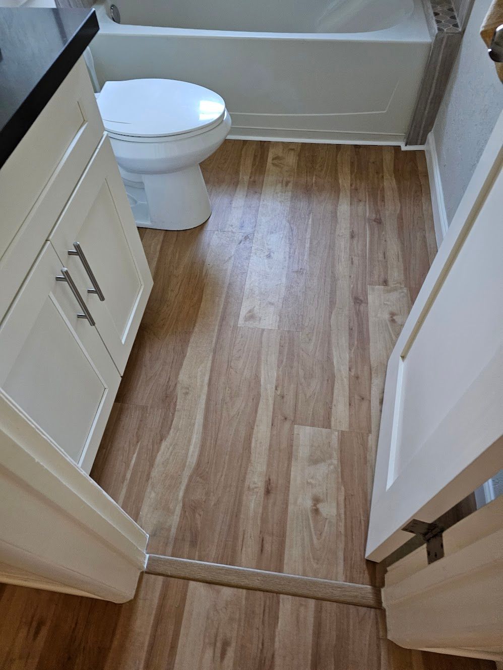 Bathroom with wood-look floor, white vanity, toilet, and bathtub.