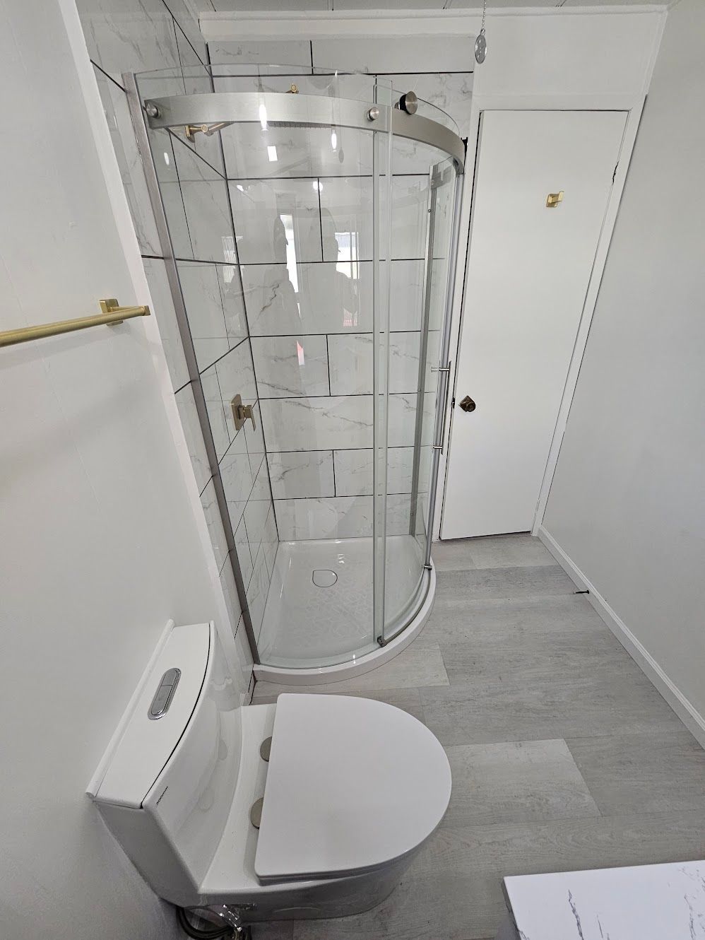 Small bathroom with a toilet, curved glass shower, and white door.