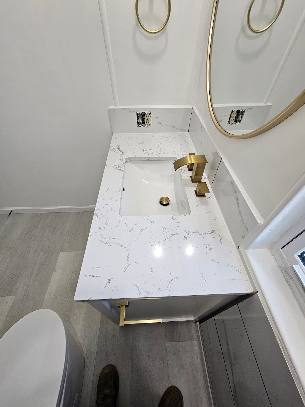 Small bathroom with white countertop, gold fixtures, and gray floors.