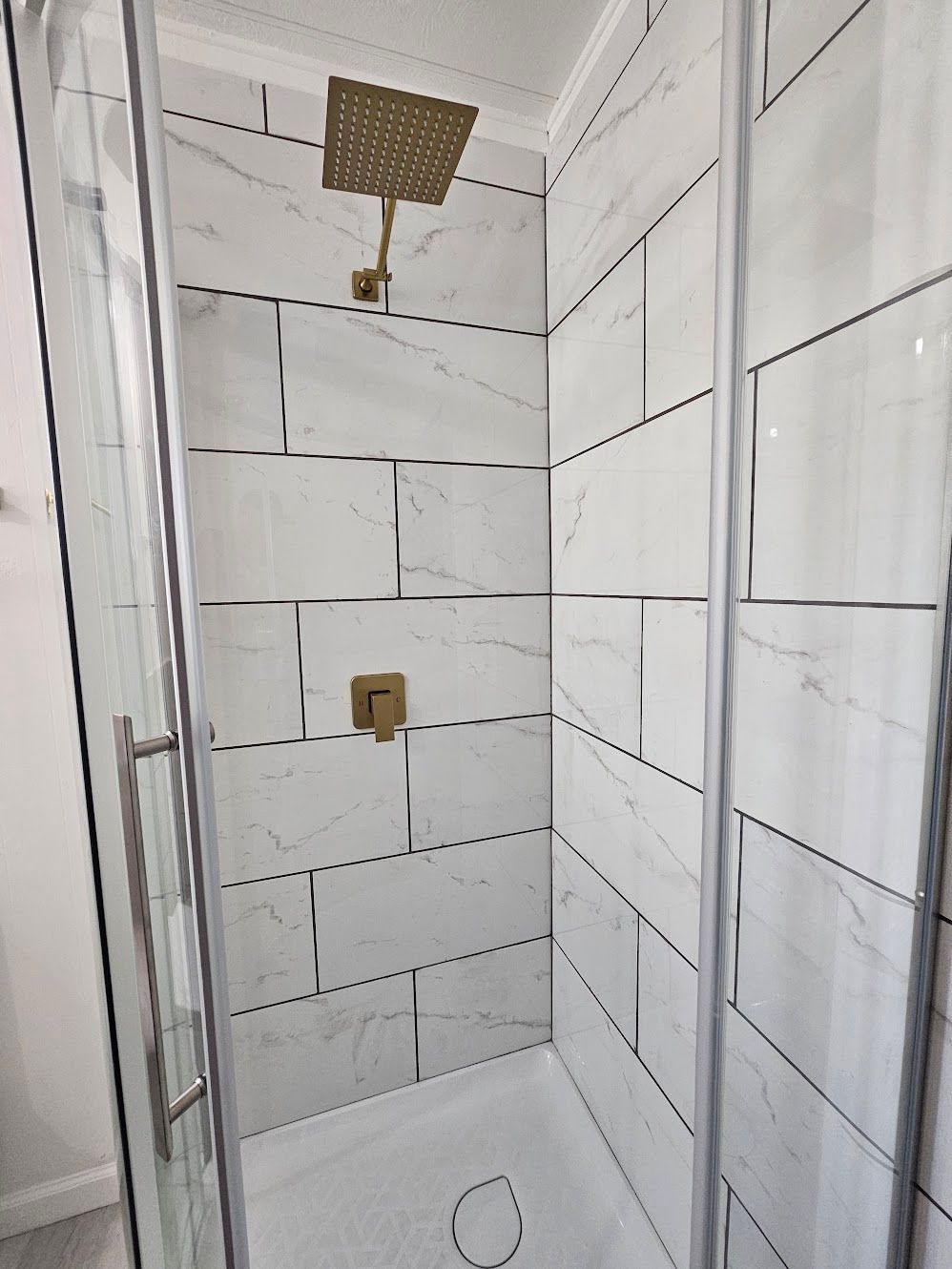 Shower stall with white marble-look tiles, gold fixtures, and glass doors.