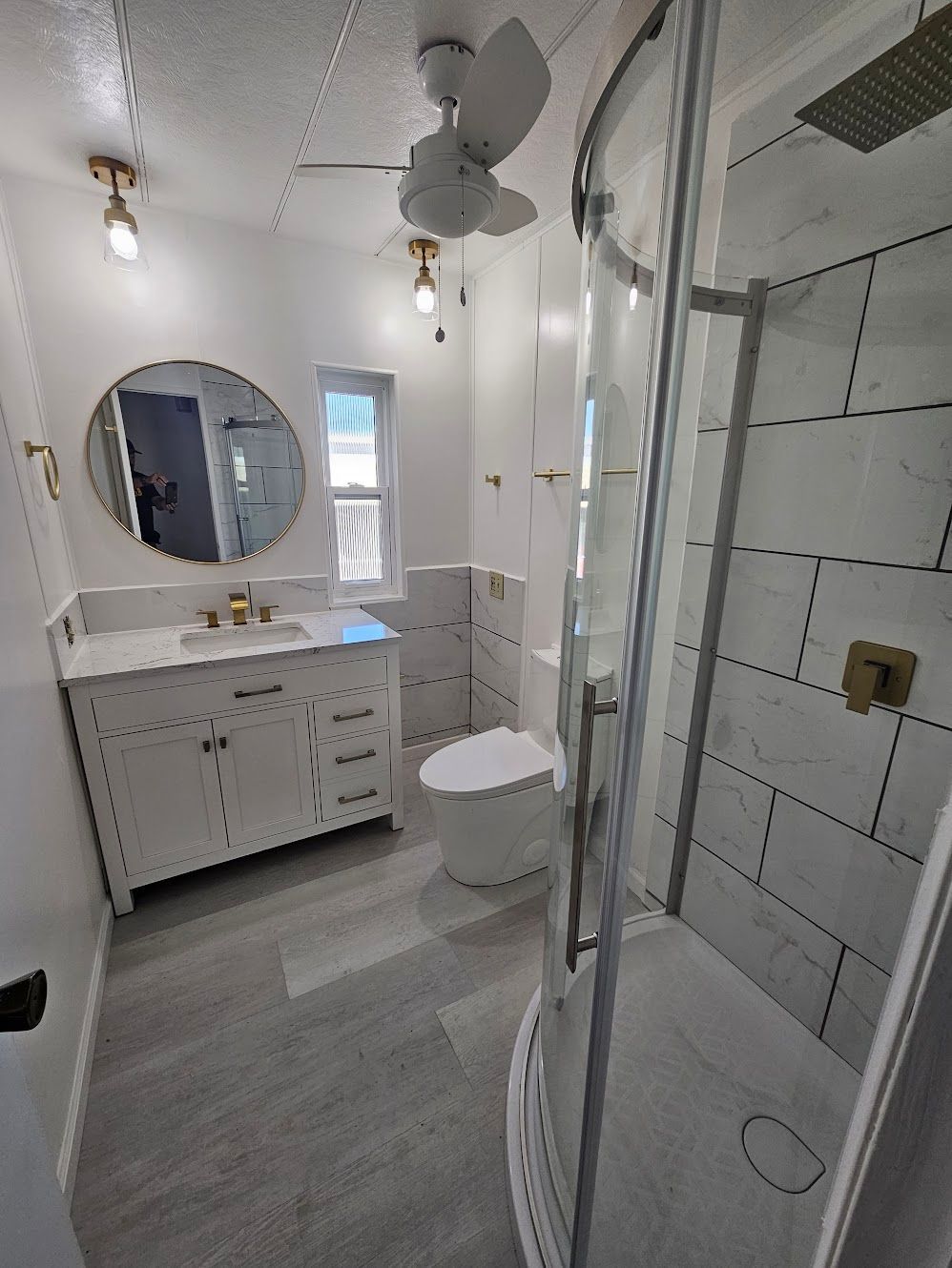 Newly renovated bathroom with white and gold fixtures, a large shower, and a modern toilet.