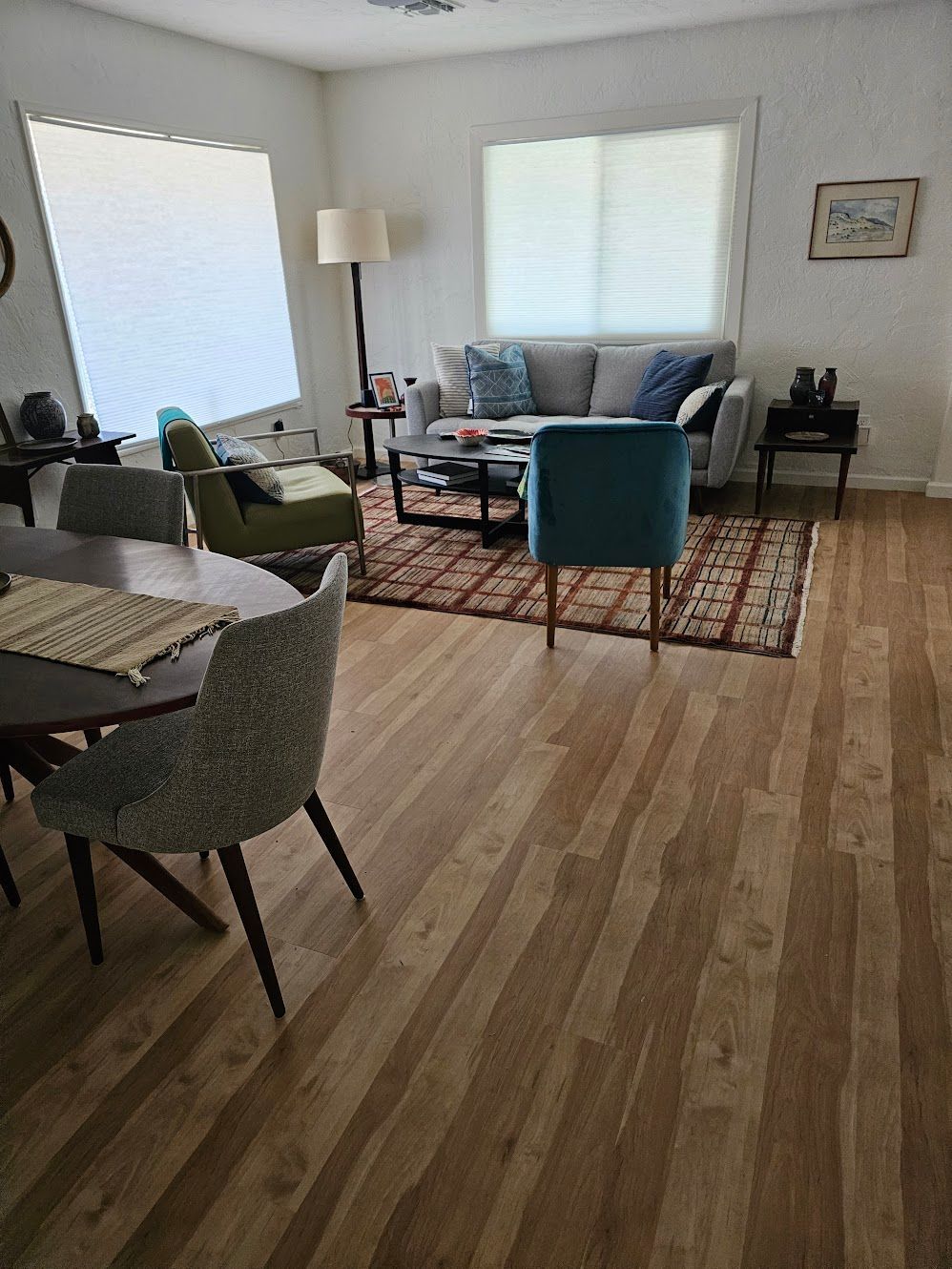 Living room with gray sofa, teal chair, rug, wood floor, round dining table with chairs.