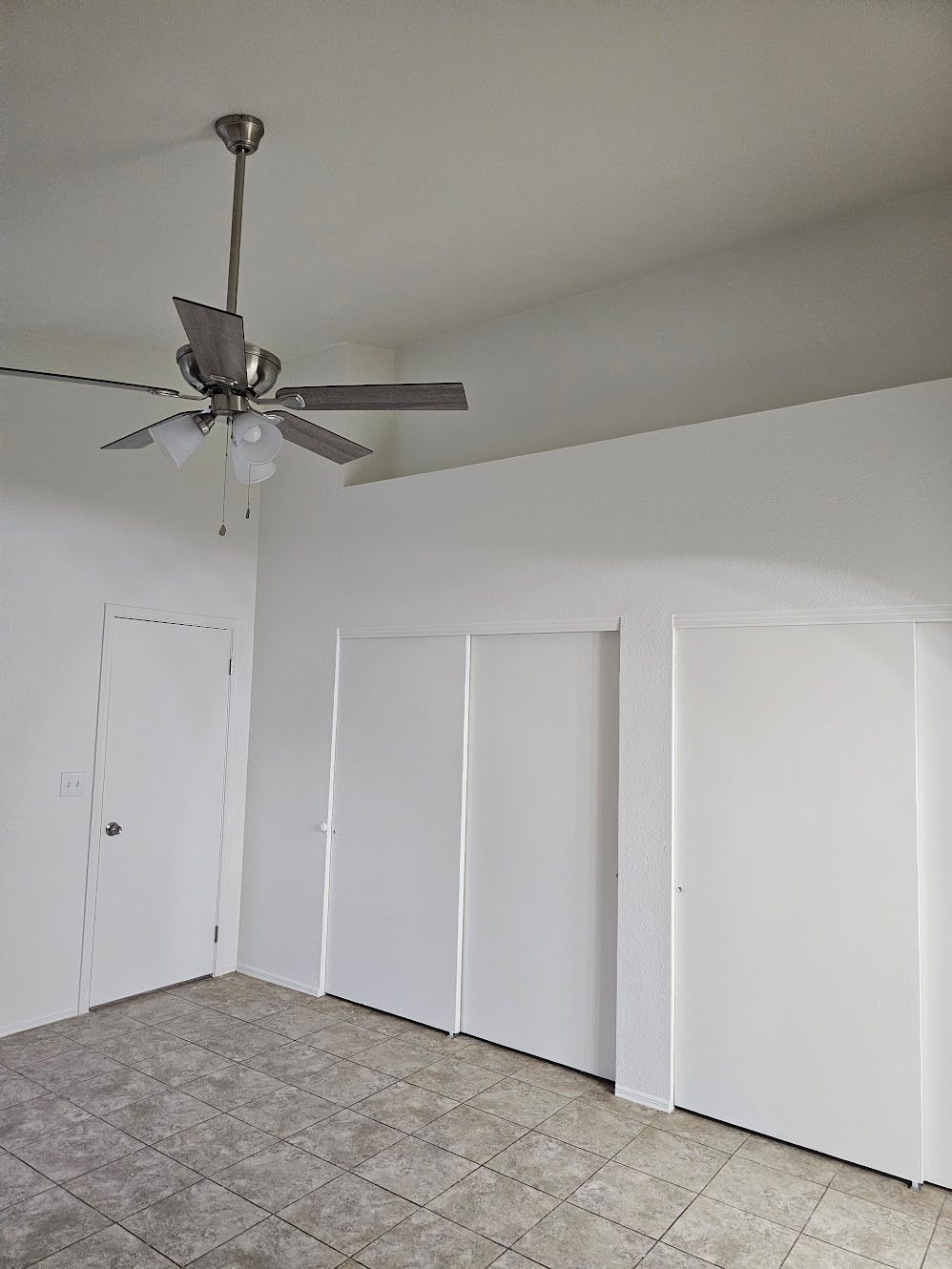 Empty room with a ceiling fan, closed closet doors, and a door on the left side.