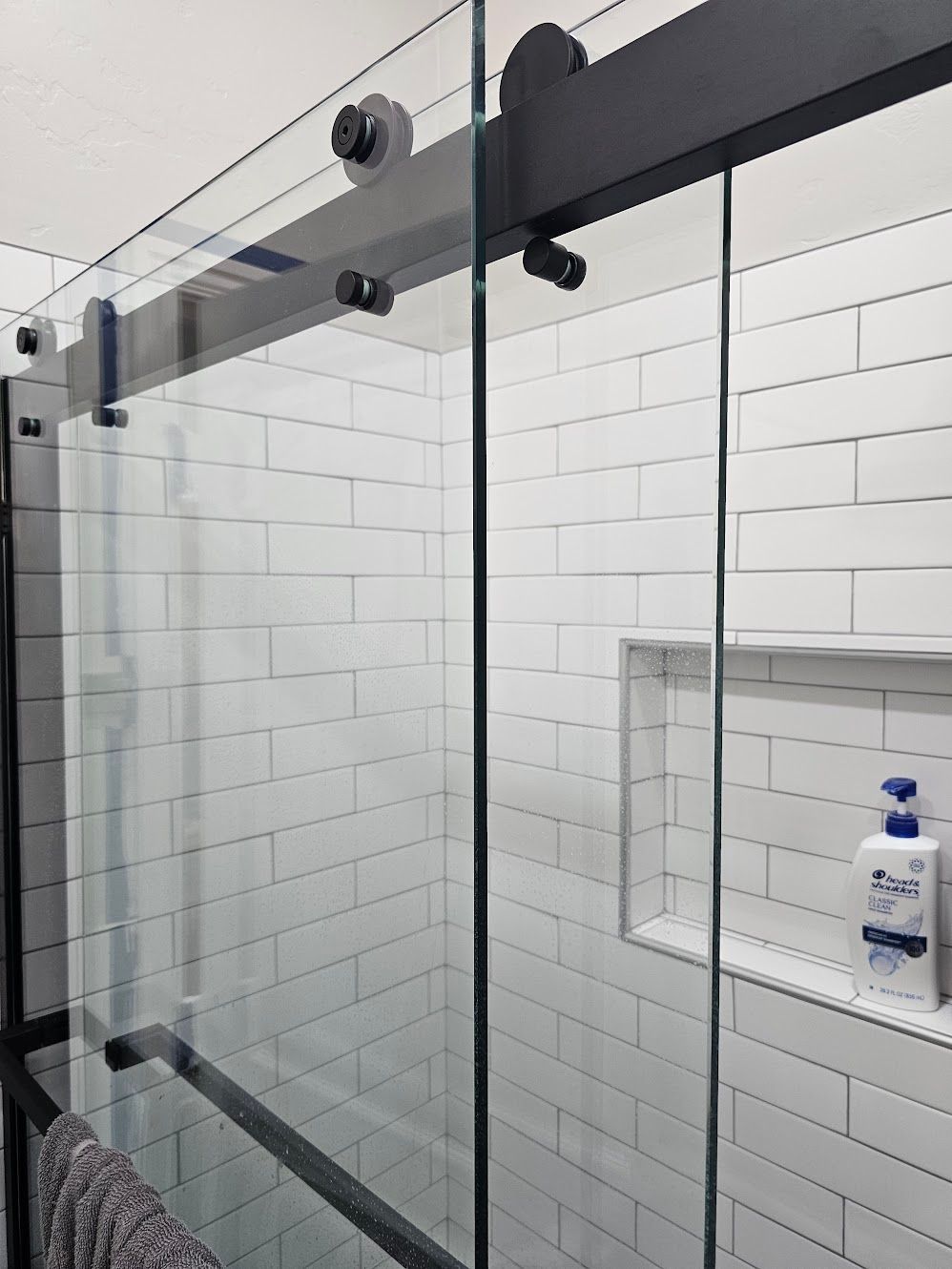 Black framed sliding glass shower door with white subway tile.