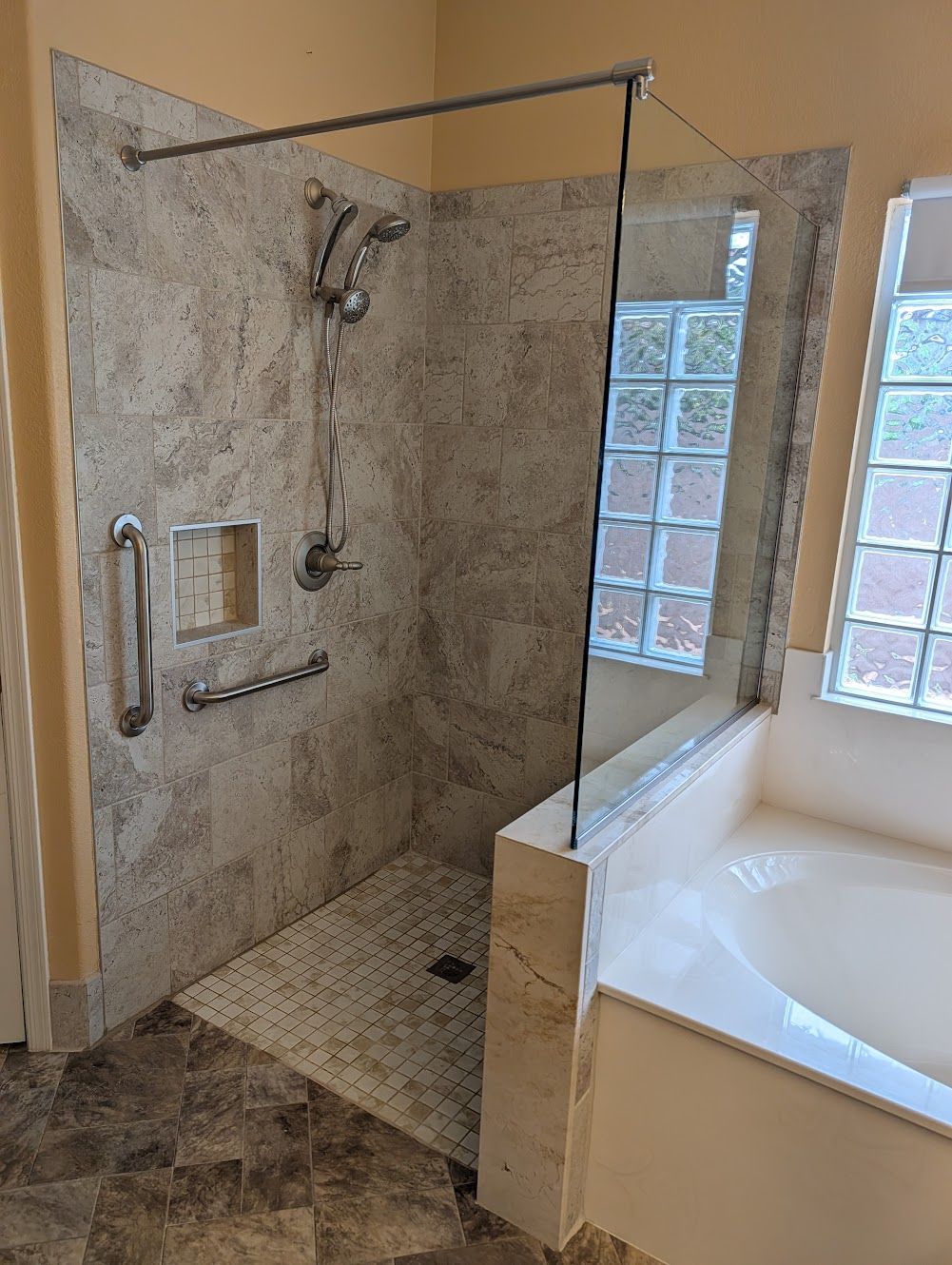 Accessible shower with tile walls, grab bars, and glass enclosure adjacent to a bathtub.