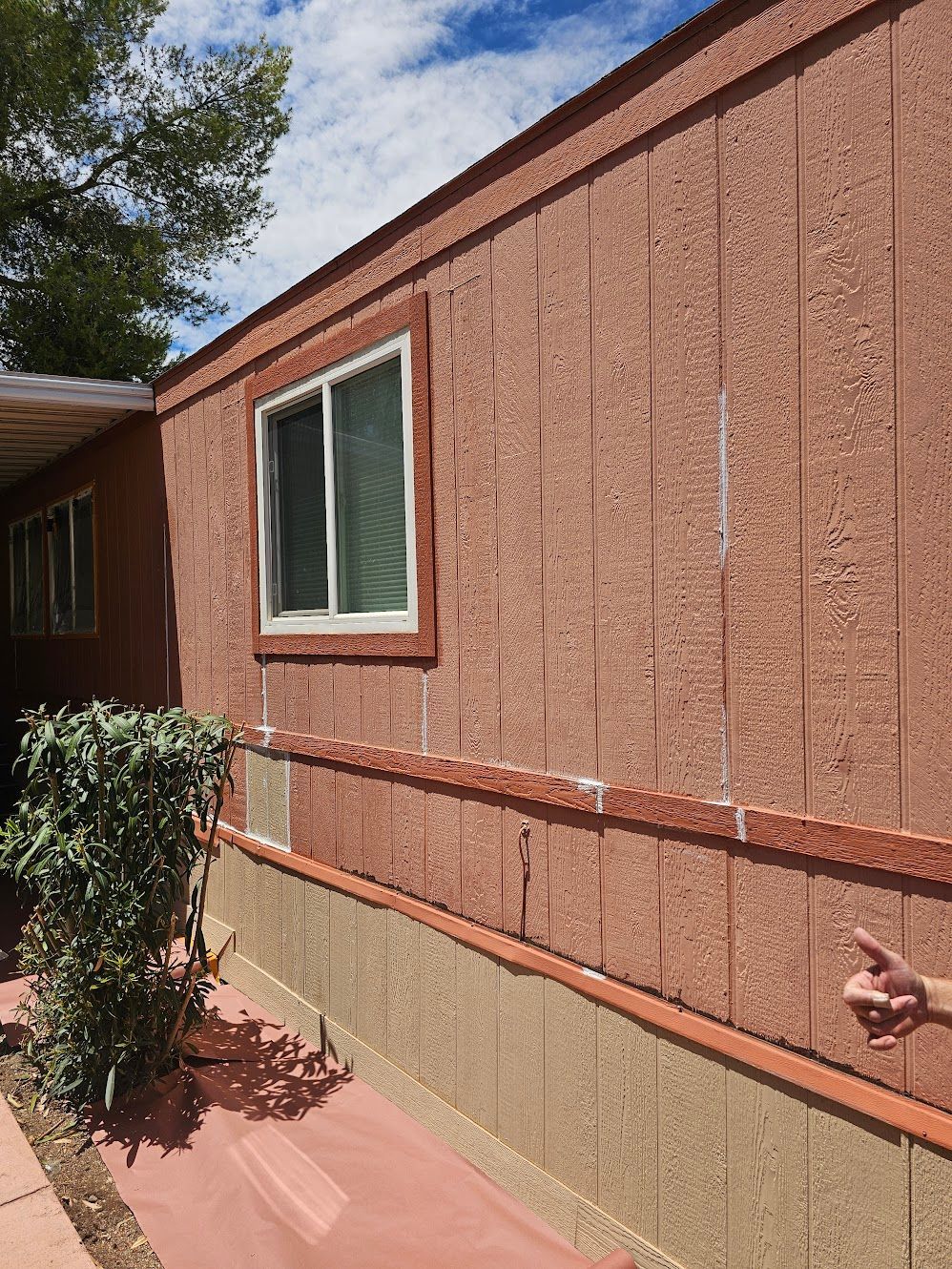 Red mobile home exterior with a white-framed window, textured siding, and a low brick foundation.