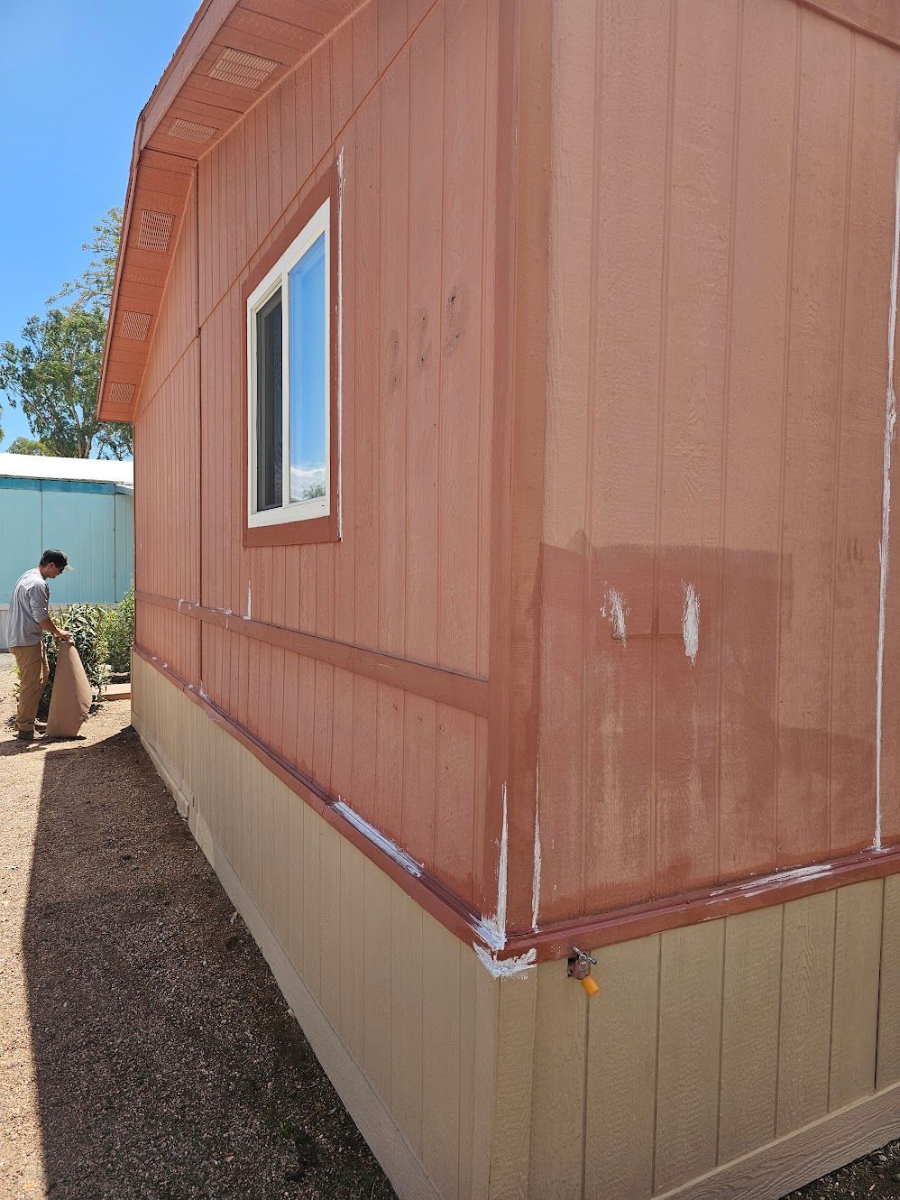 Exterior of a building with peeling orange paint; a person works nearby; a window is visible.