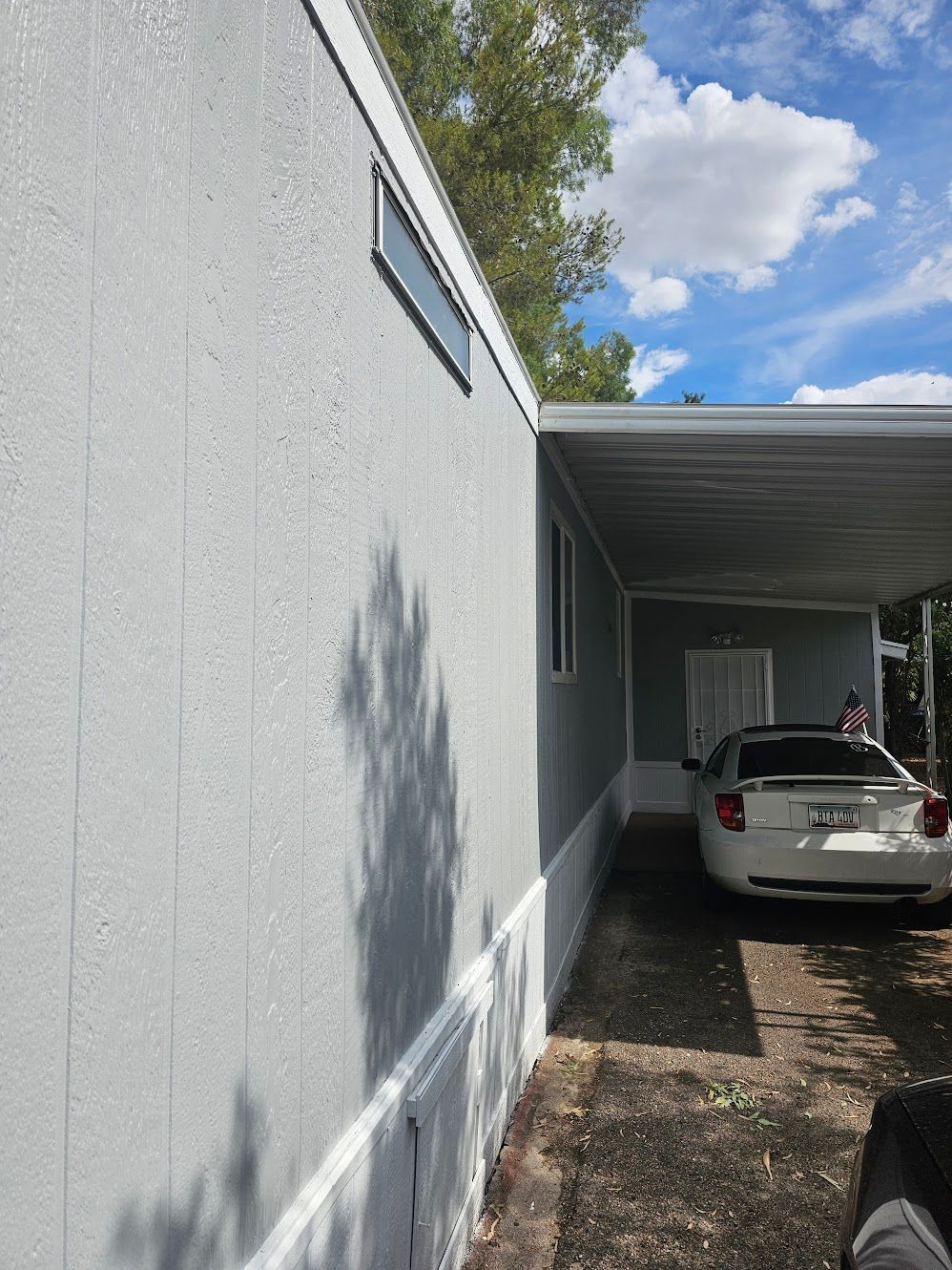 Gray mobile home exterior with a carport and a white car.