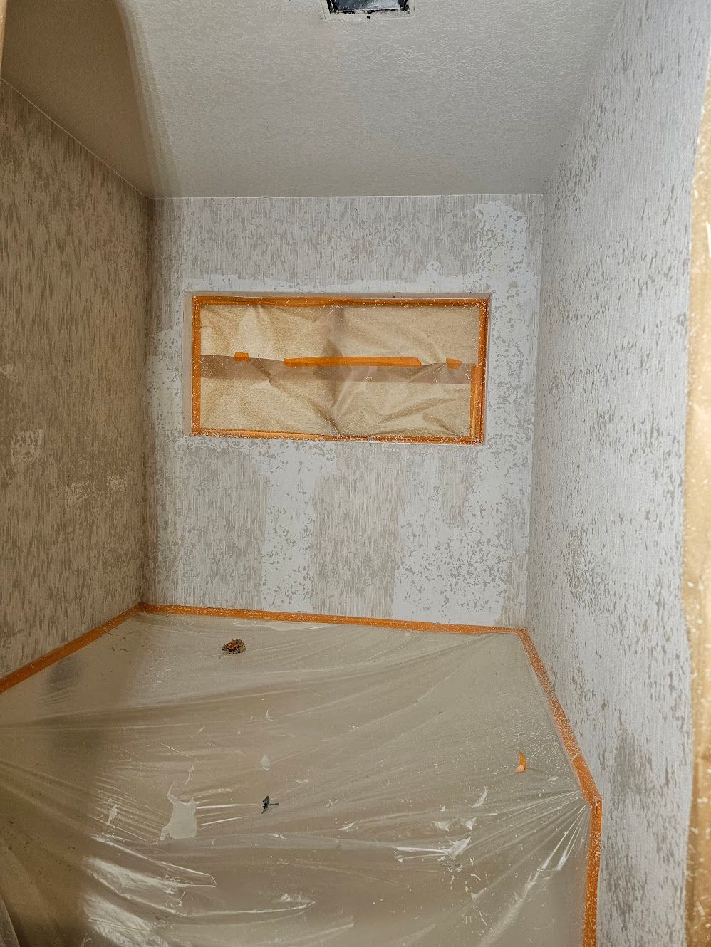 A small room with speckled walls, taped window, and plastic sheeting on the floor.