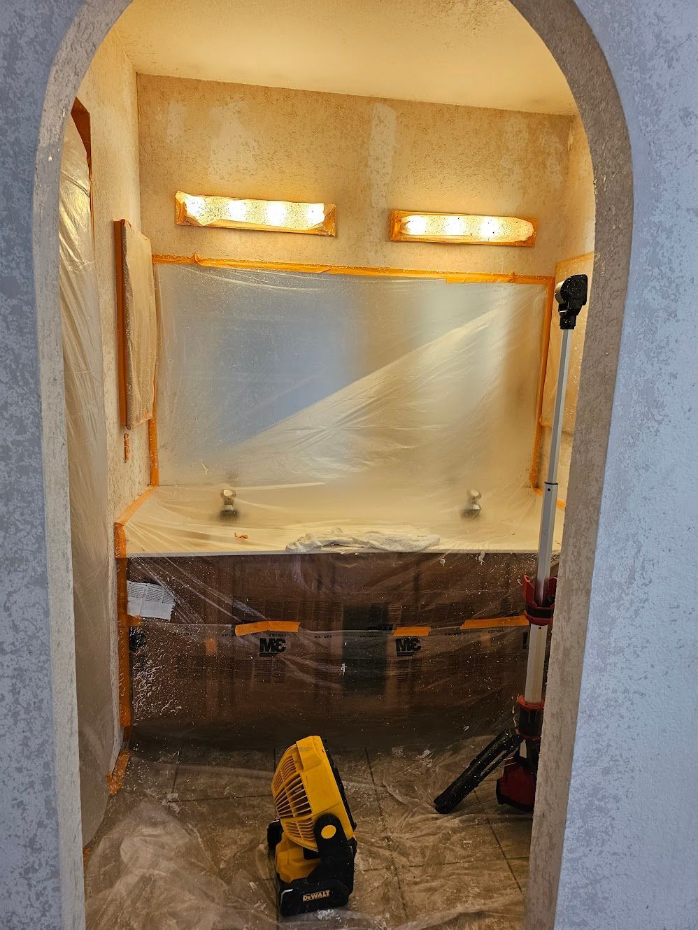 Bathroom niche under renovation, covered in plastic, with lights and work light visible.