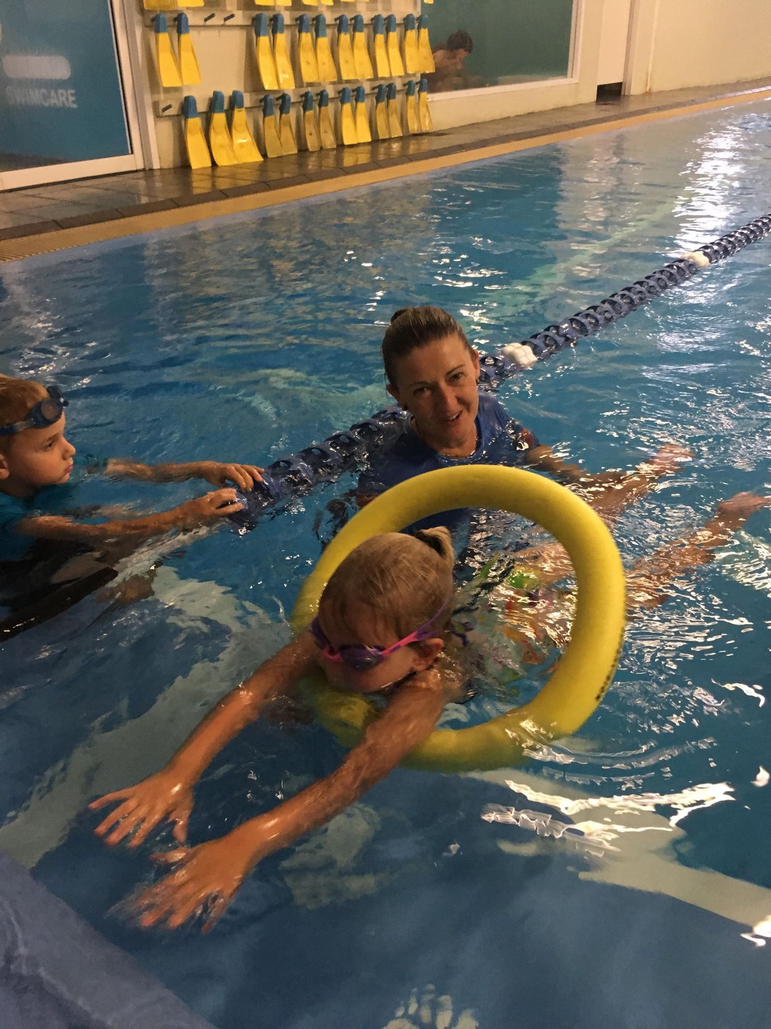 Child in a Pool With a Swim Noodle, Instructed by an Adult. Another Child is Nearby — Swim Care Boambee in Coffs Harbour, NSW