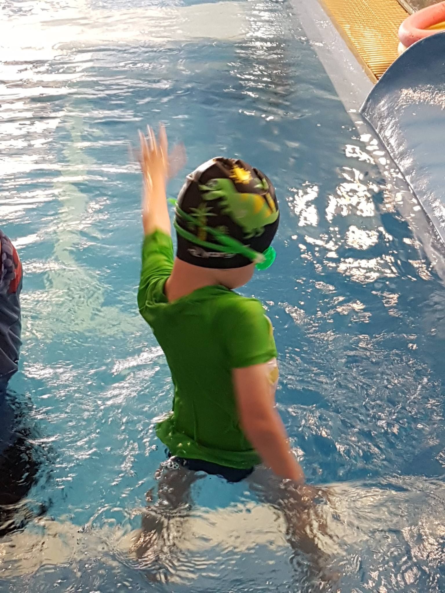 Child in Green Shirt and Swim Cap Waves from Pool — Swim Care Boambee in Coffs Harbour, NSW
