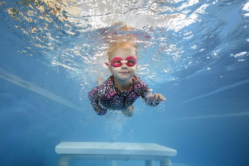 Child Swimming Underwater, Wearing Goggles and Rash Guard, Smiling — Swim Care Boambee in Coffs Harbour, NSW