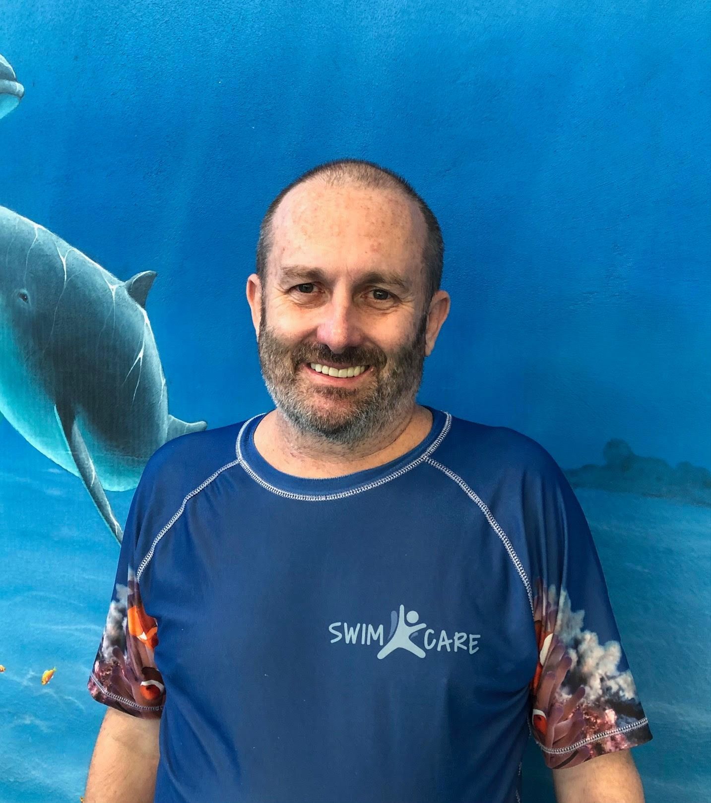 A swim instructor is standing in front of a wall while wearing Swim Care Swim shirt — Swim Care Boambee in Coffs Harbour, NSW