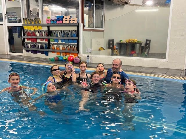 Group of children and a man smiling in a swimming pool — Swim Care Boambee in Coffs Harbour, NSW