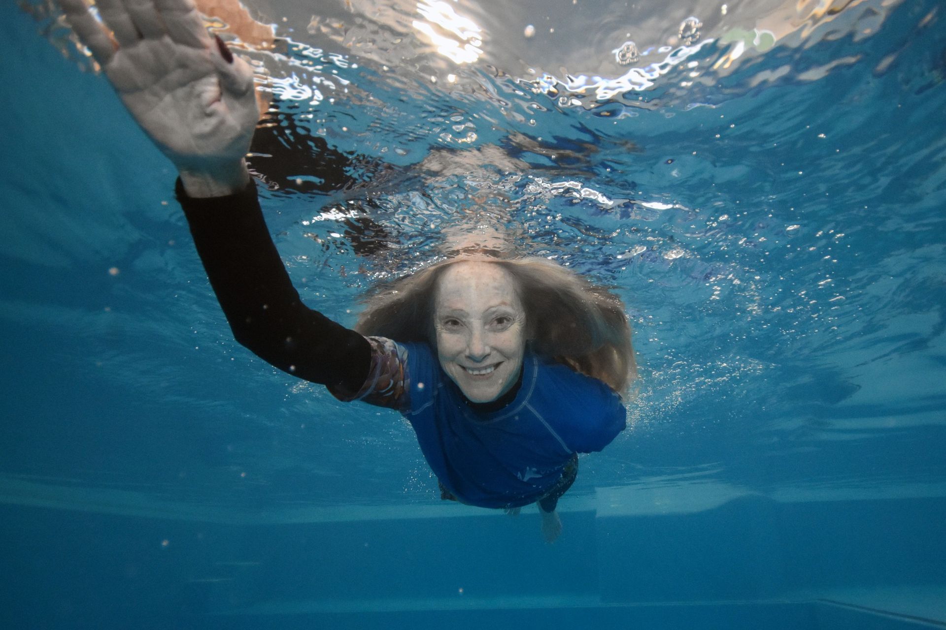 Woman Swims Underwater, Smiling, Reaches With Her Arm — Swim Care Boambee in Coffs Harbour, NSW
