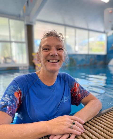 A women is in a pool while smiling and wearing a swim care shirt — Swim Care Boambee in Coffs Harbour, NSW