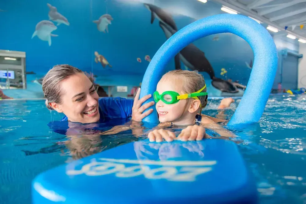 Instructor Helping a Child in a Pool With a Float. the Child Wears Goggles — Swim Care Boambee in Coffs Harbour, NSW