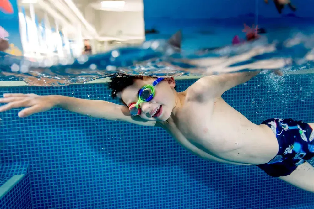 A Kid Is Swimming in A Tiled Swimming Pool Wearing Goggles — Swim Care Boambee in Coffs Harbour, NSW