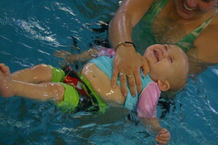 Baby In Pool Held by Adult, Smiling, Wearing Swimsuit — Swim Care Boambee in Coffs Harbour, NSW