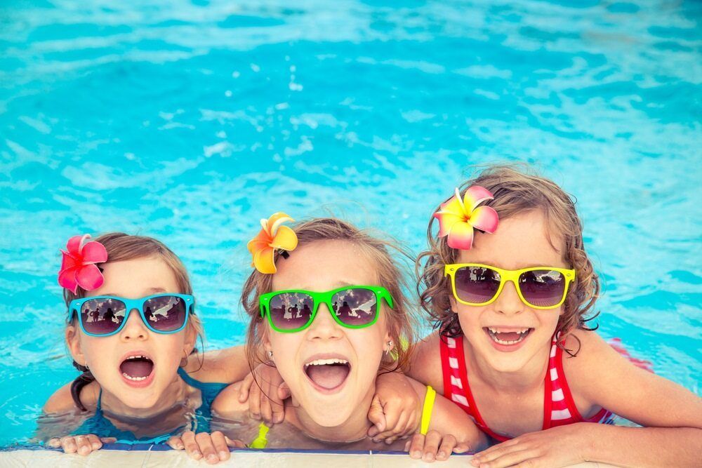 Three Children in A Pool, Wearing Sunglasses and Flower Hair Accessories, Smiling — Swim Care Boambee in Coffs Harbour, NSW