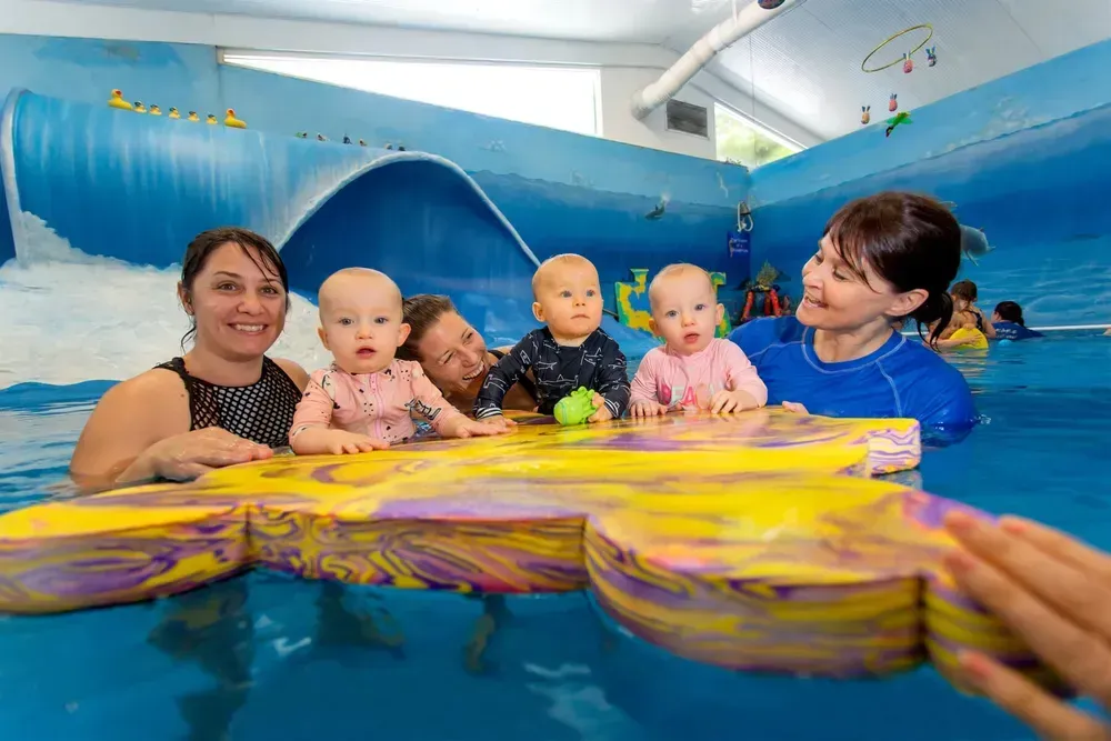 People and Babies in a Wave Pool. Babies Sit on a Yellow Float, Adults Smile — Swim Care Boambee in Boambee, NSW