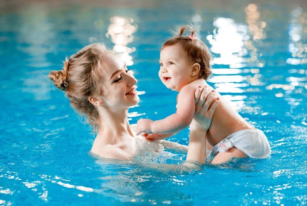 Woman and Baby Playing in A Blue Pool; Woman Holds Baby, Both Smiling — Swim Care Boambee in Coffs Harbour, NSW