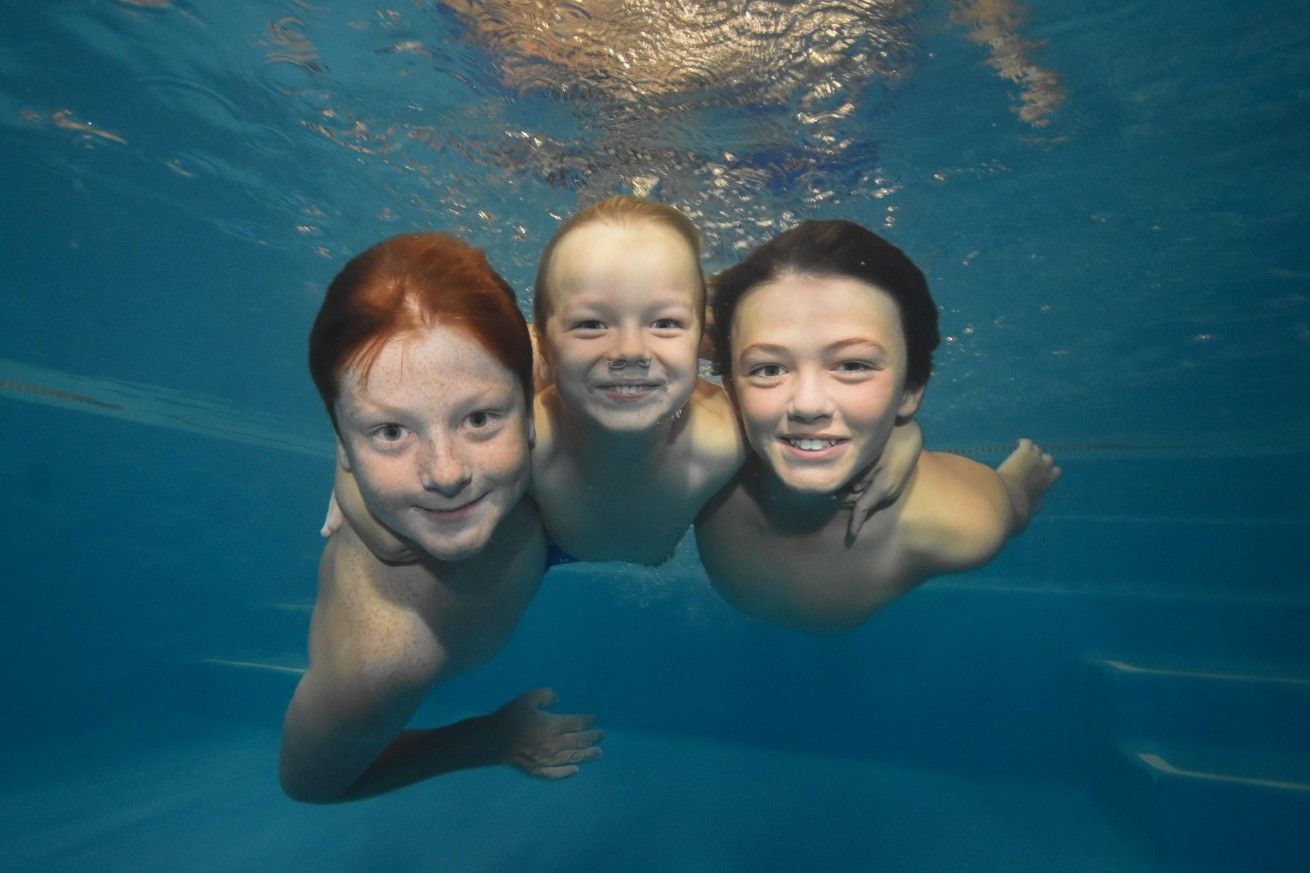 Three Children Underwater Smiling With Arms Around Each Other — Swim Care Boambee in Harbour, NSW