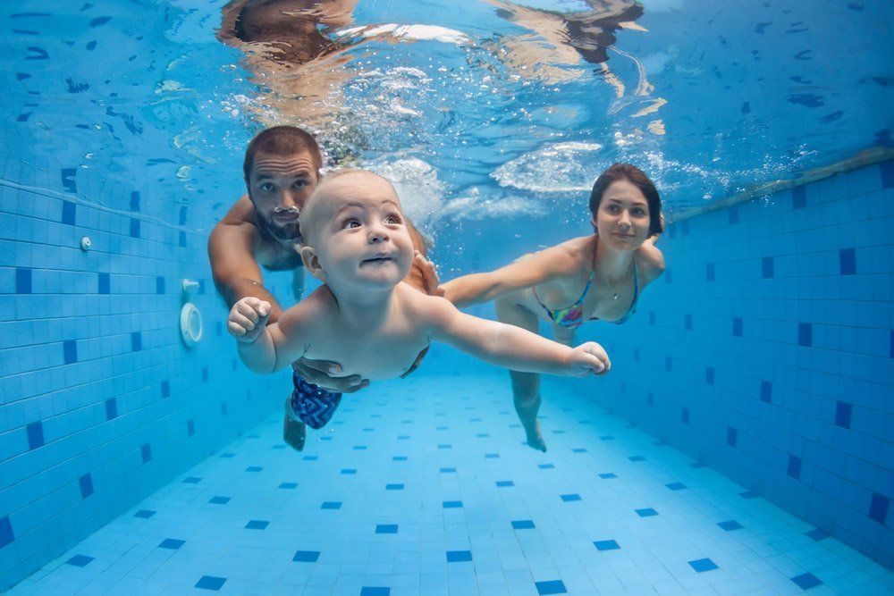 Family Swimming Underwater with Baby in Blue Tiled Pool — Swim Care Boambee in Coffs Harbour, NSW