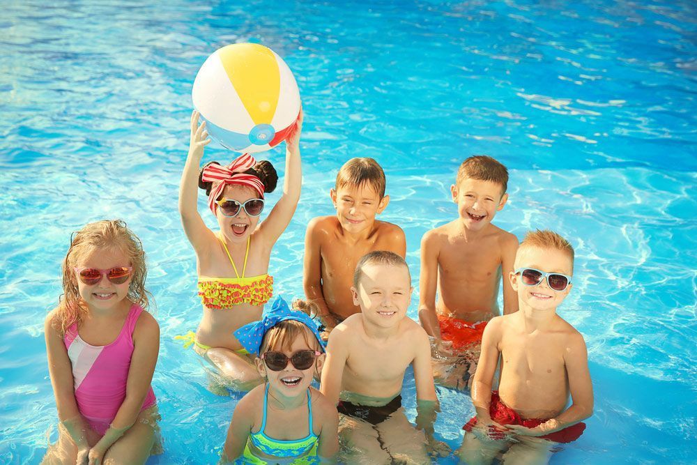Children in A Pool, Holding a Beach Ball. the Kids Are Smiling and Wearing Swimwear and Sunglasses — Swim Care Boambee in Coffs Harbour, NSW