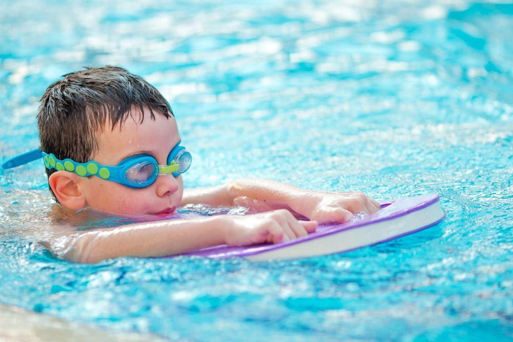 Boy in Swimming Goggles Using a Kickboard in A Pool — Swim Care Boambee in Coffs Harbour, NSW