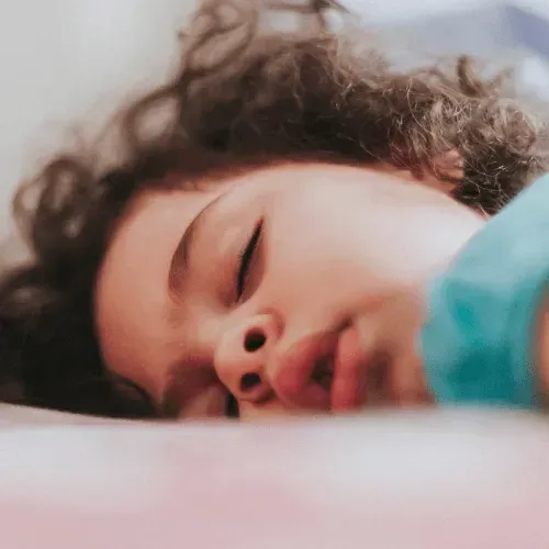 A Person with Curly Hair Sleeping, Face Close up On a Pink Surface — Swim Care Boambee in Coffs Harbour, NSW