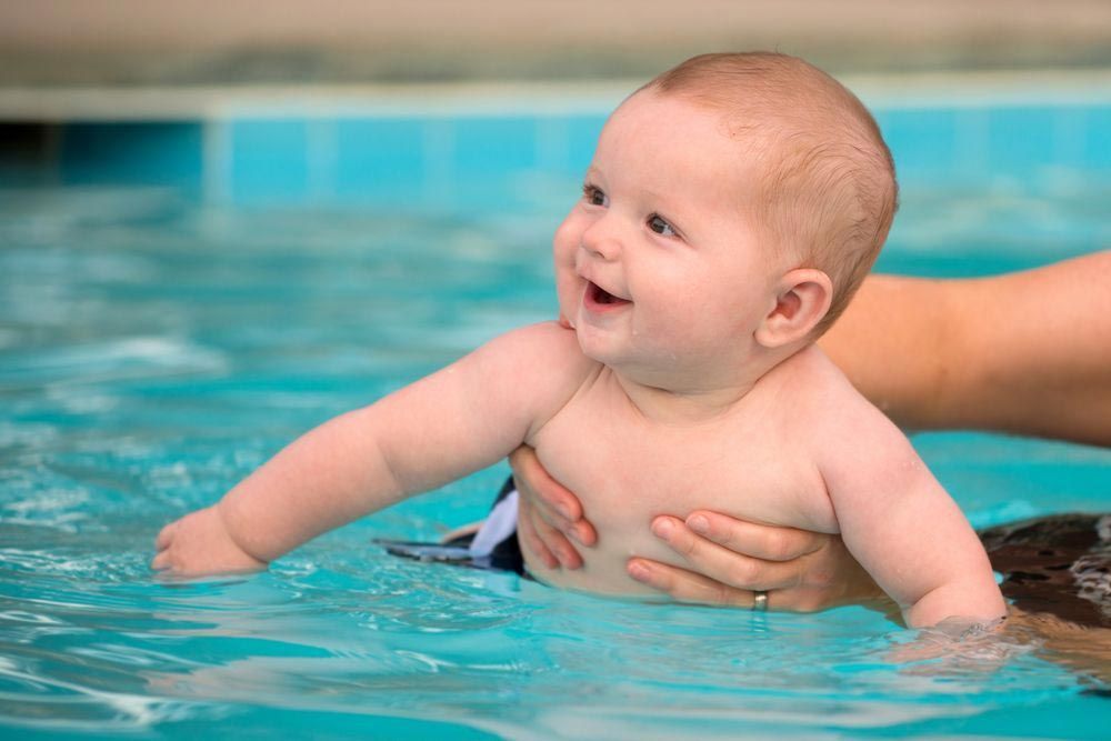 Baby in A Pool, Smiling and Being Held by A Person's Arms in The Water — Swim Care Boambee in Coffs Harbour, NSW