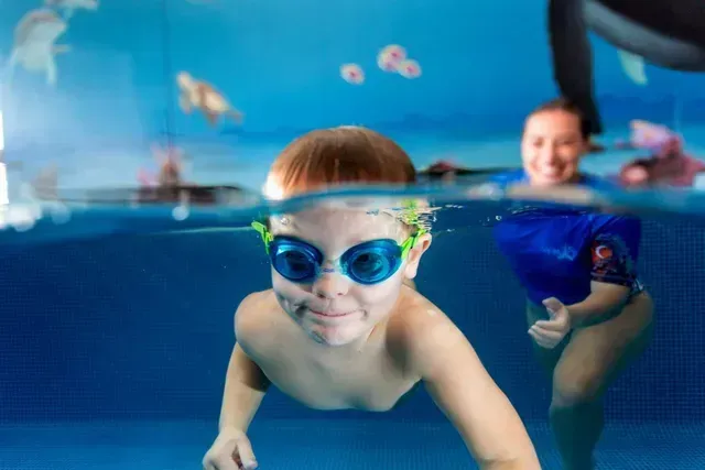 Boy With Goggles Smiling Underwater in a Blue Pool — Swim Care Boambee in Harbour, NSW