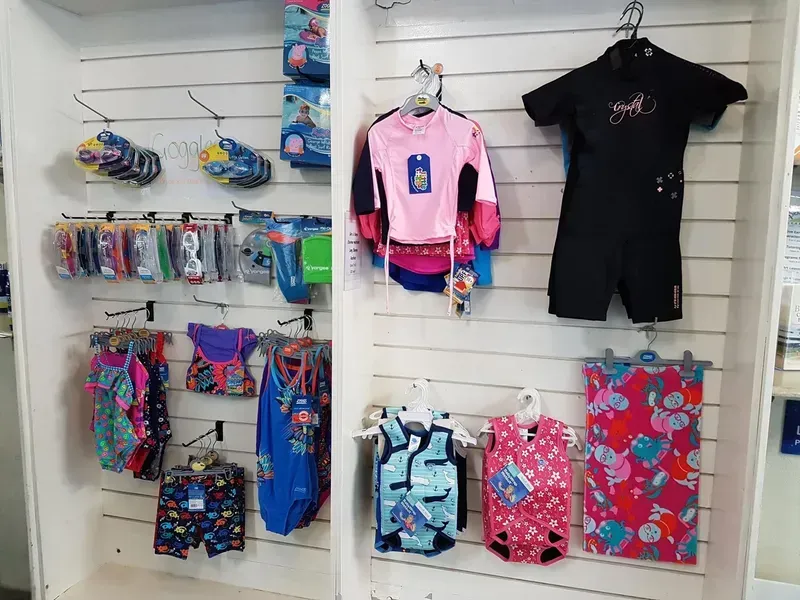 Swimwear Display: Various Swimsuits, Goggles, and Wetsuits on Hangers in A Shop — Swim Care Boambee in Coffs Harbour, NSW