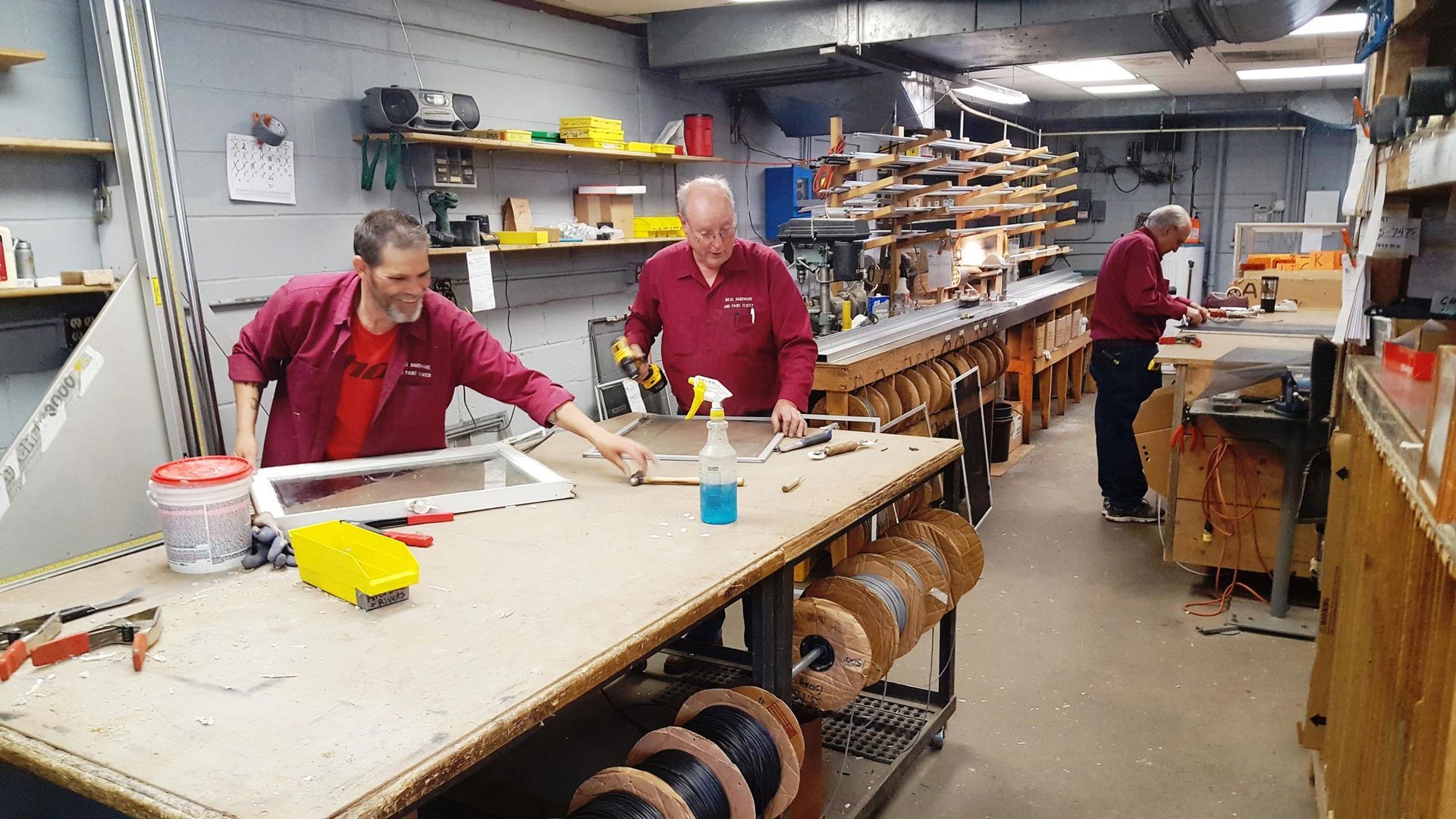 Three men work at a workbench in a workshop, repairing window frames.