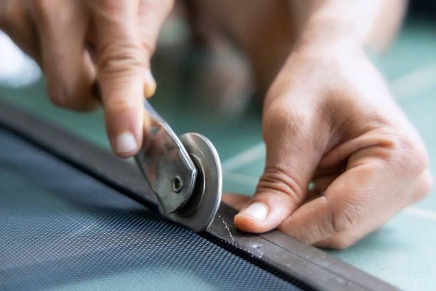 Hands using a spline roller to secure mesh during a window screen repair.