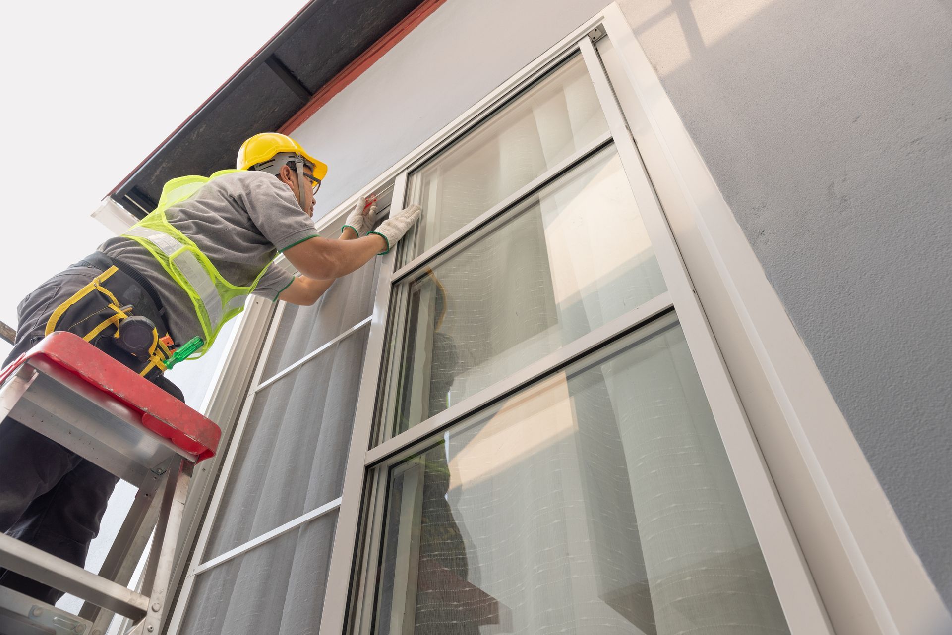 A worker, in protective gear, is performing residential window repair on a sliding window.