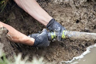 a person is fixing a pipe in the mud .