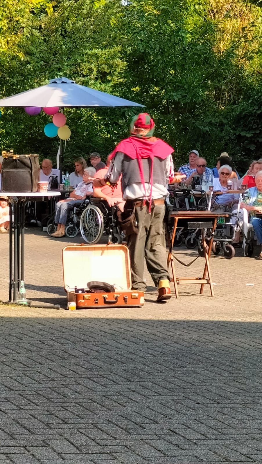 Ein Mann steht neben einem Koffer vor einer Gruppe von Menschen im Rollstuhl.