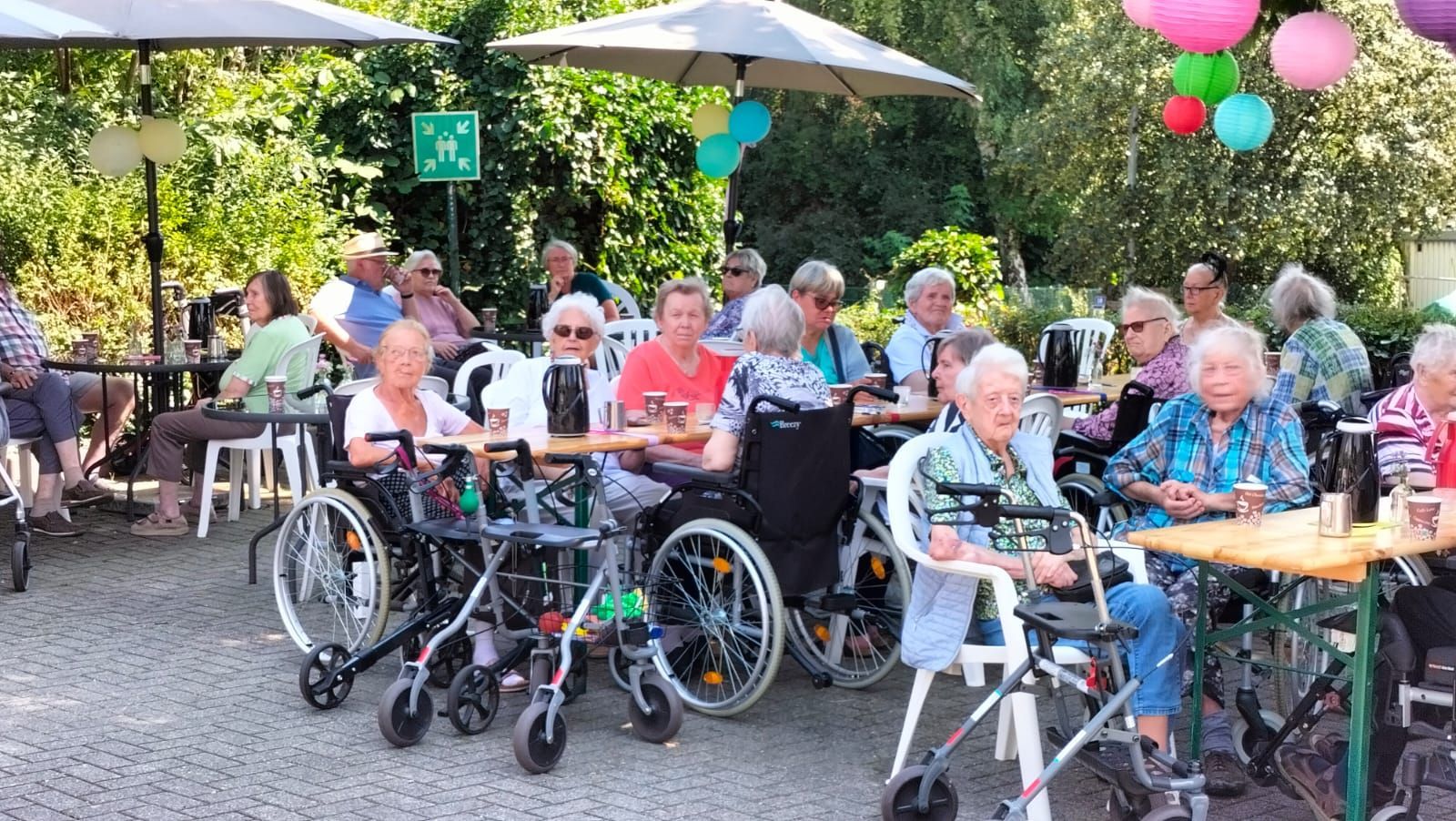 Eine Gruppe von Menschen im Rollstuhl sitzt an Tischen unter Sonnenschirmen.
