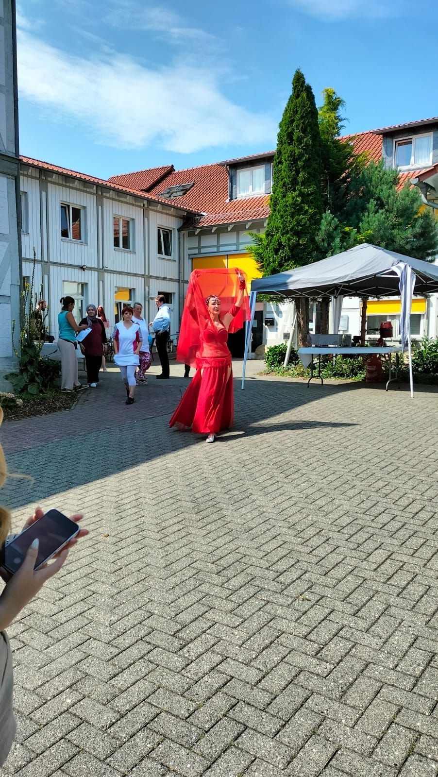 Eine Frau in einem roten Kleid läuft mit einem Regenschirm in der Hand einen Gehweg aus Backsteinen entlang.