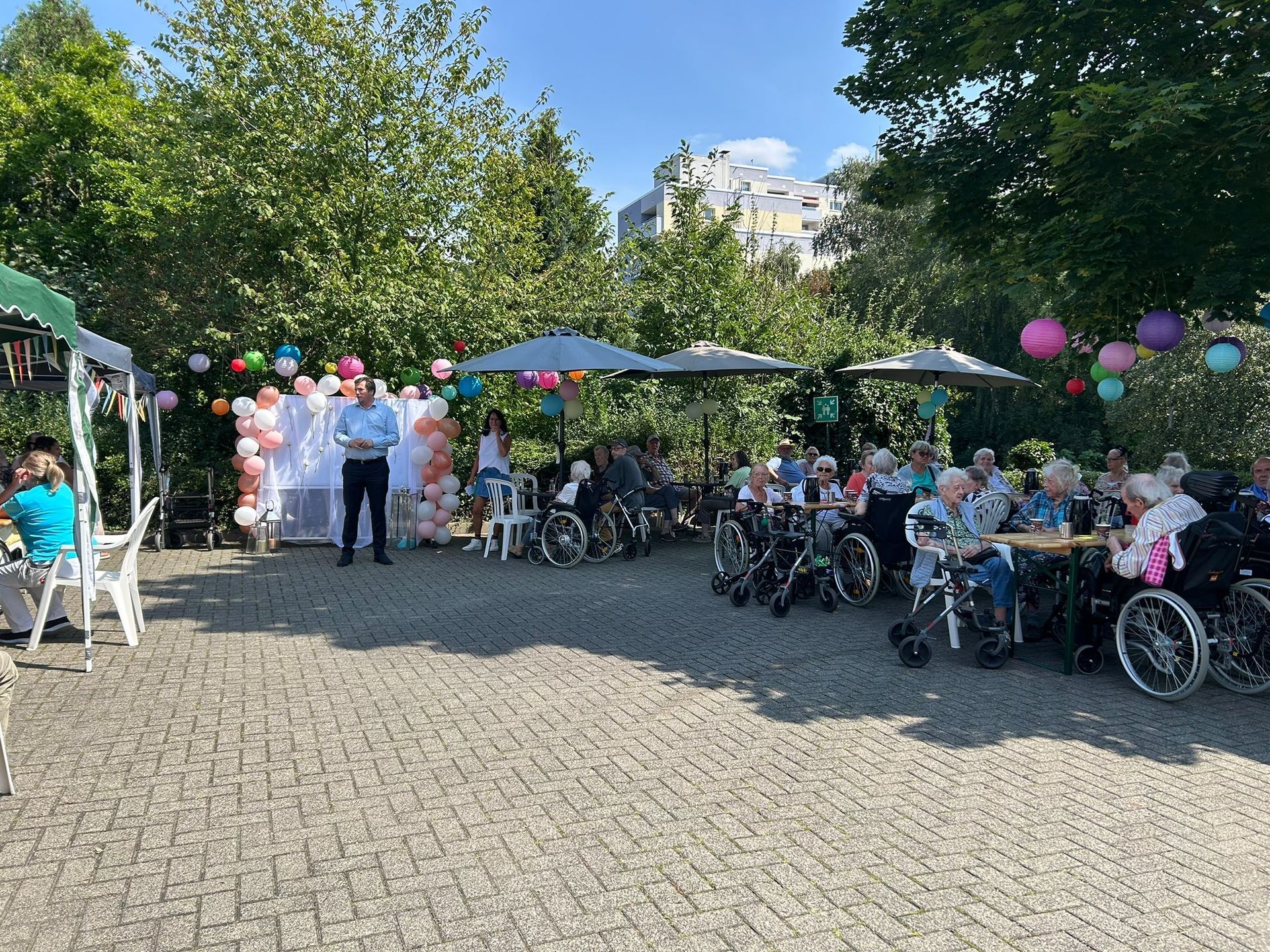 Eine Gruppe von Menschen im Rollstuhl sitzt unter Sonnenschirmen in einem Park.