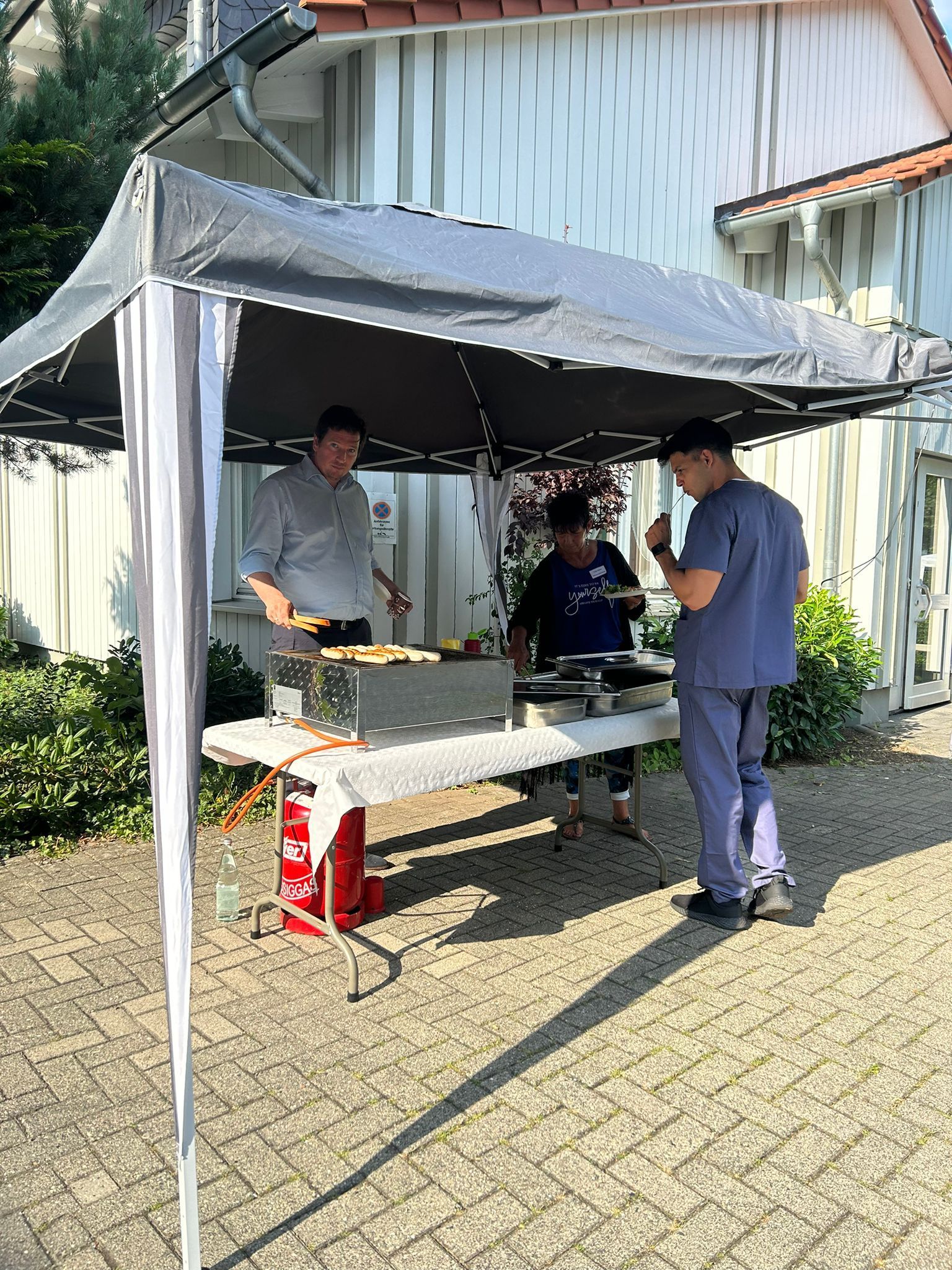 Eine Gruppe von Leuten steht unter einem Zelt um einen Tisch herum.